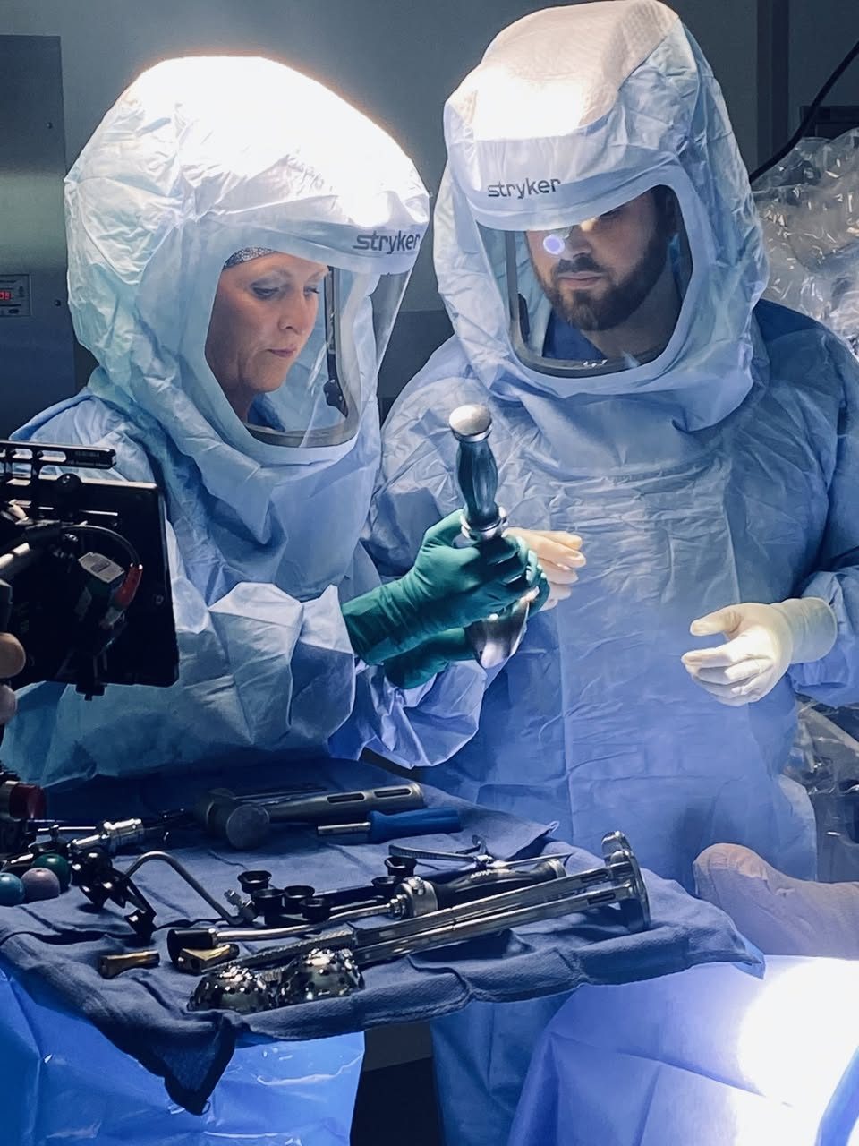 Dr. MacNeille and a surgical team member in sterile hoods examining a hip implant over a table of joint replacement instruments